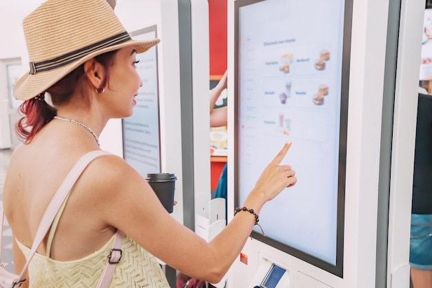 A female customer uses a touchscreen terminal or selfservice kiosk to order at a fast food restaurant Automated machine and electronic payment