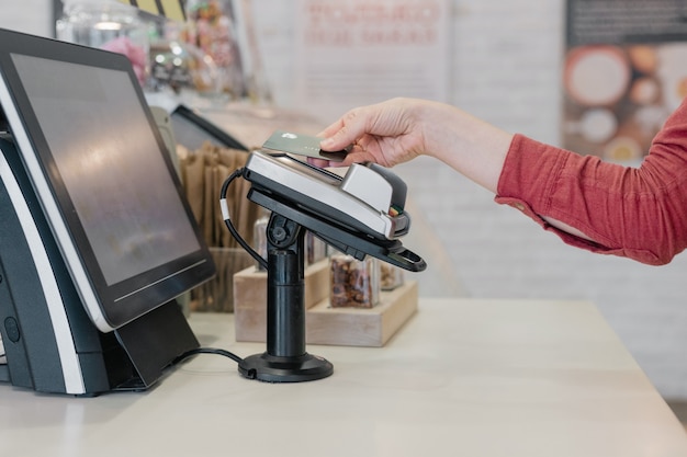 European woman paying with card at restaurant or supermarket, woman's hand holds credit card up to contactless payment terminal, online payment, cash payment, bank card purchases